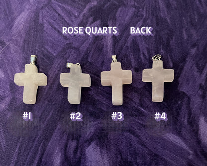 Back view of four cross-shaped rose quartz pendants on a purple textured background
