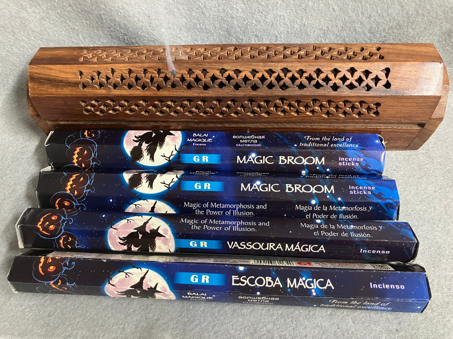 Four boxes of GR Magic Broom incense sticks if front of a decorative incense burner on a light gray background