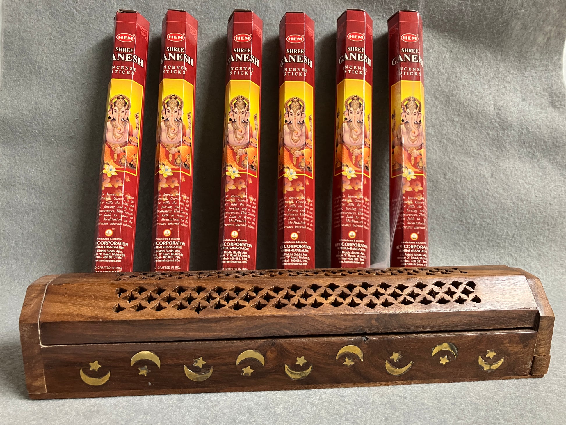 Ganesh Incense boxes shown with a wooden  incense burner on a gray background