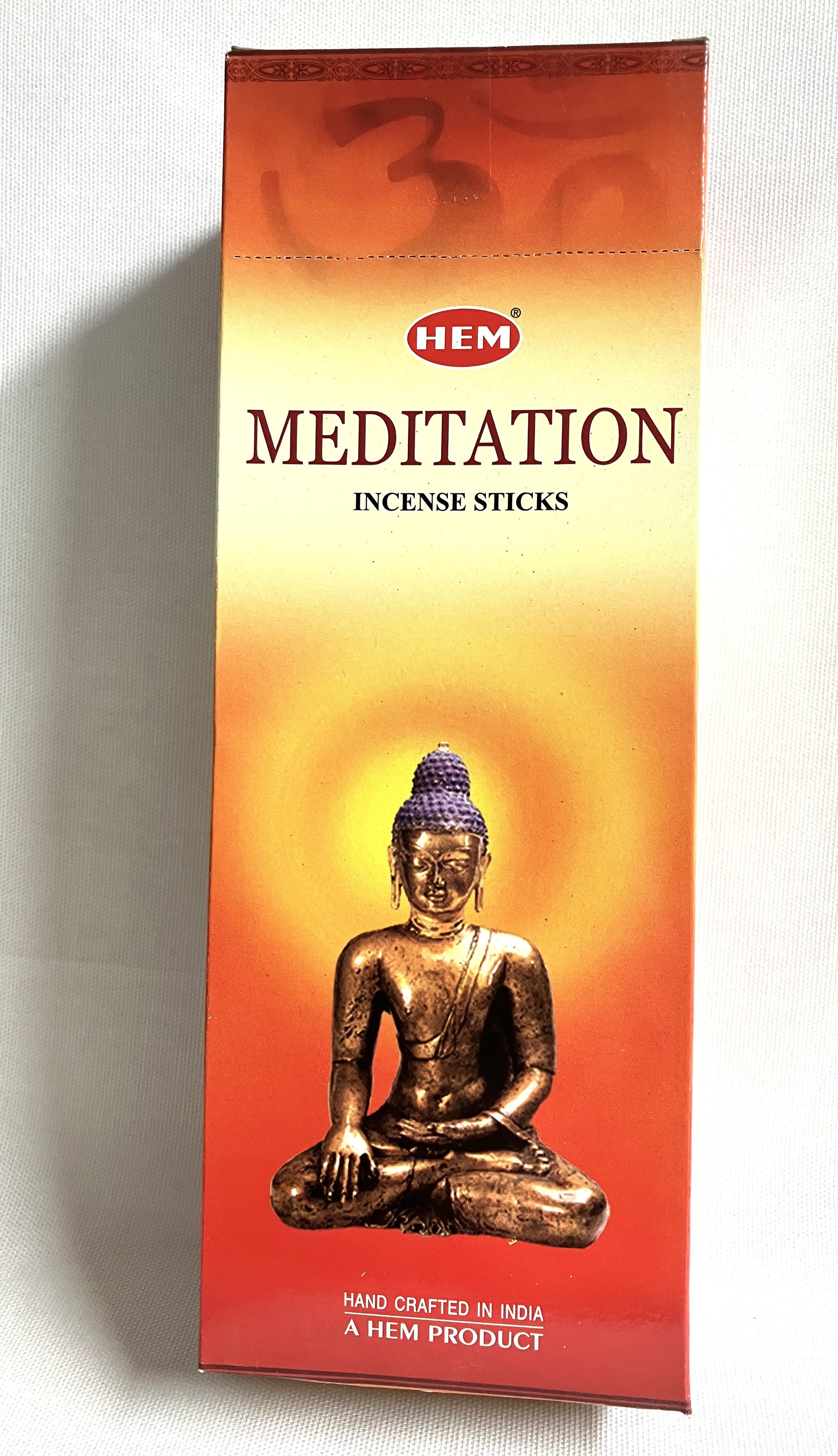 Box of HEM Meditation incense sticks with a Buddha statue on an orange background