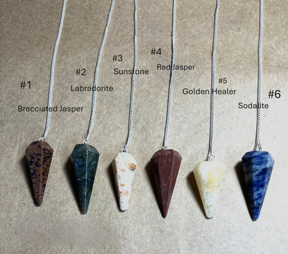 Six stone pendulums on chains with labels indicating stone type shown on a beige background