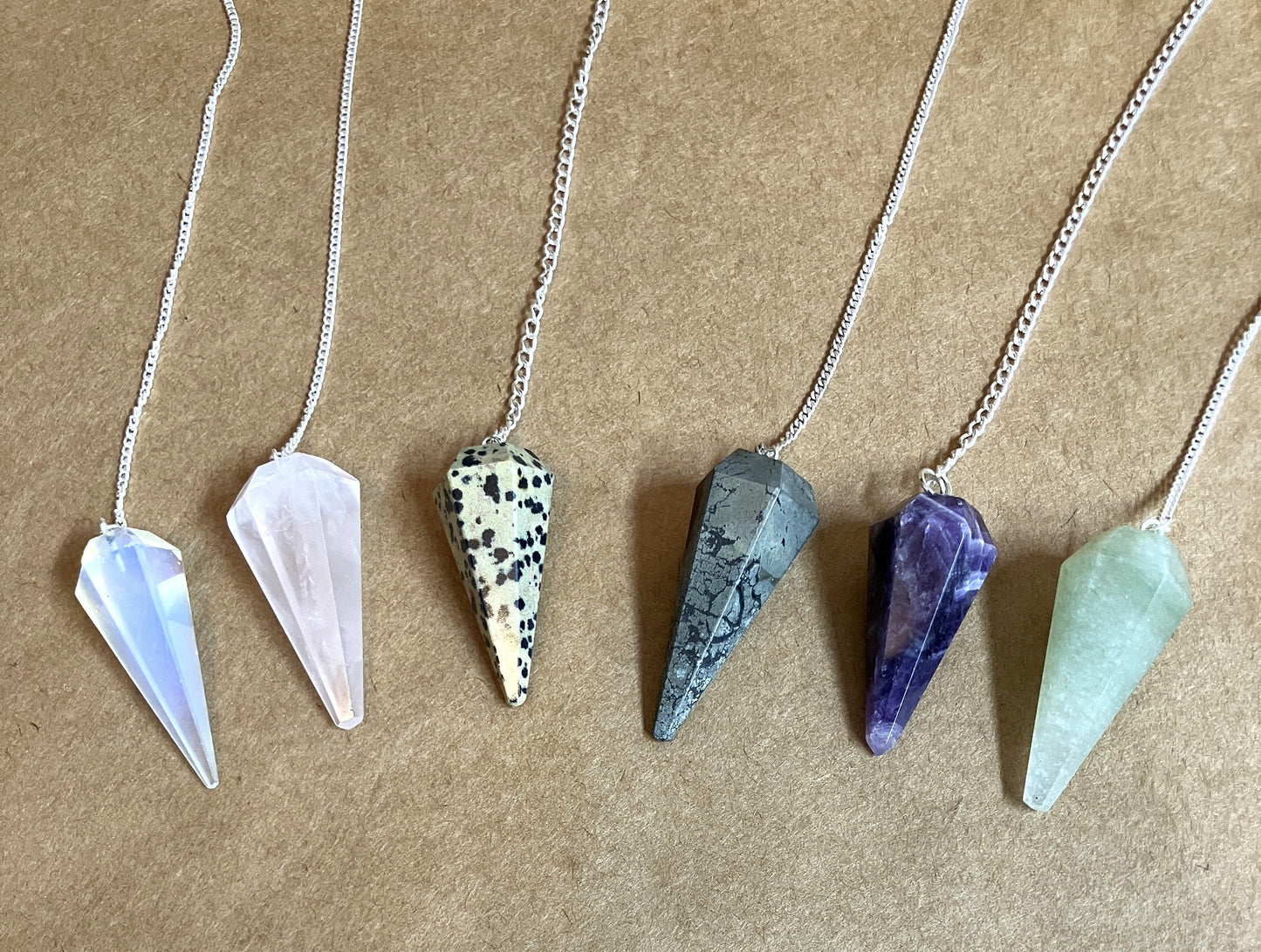 Six crystal pendulums on chains shown on a tan background