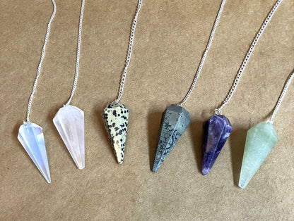 Six crystal pendulums on chains shown on a tan background