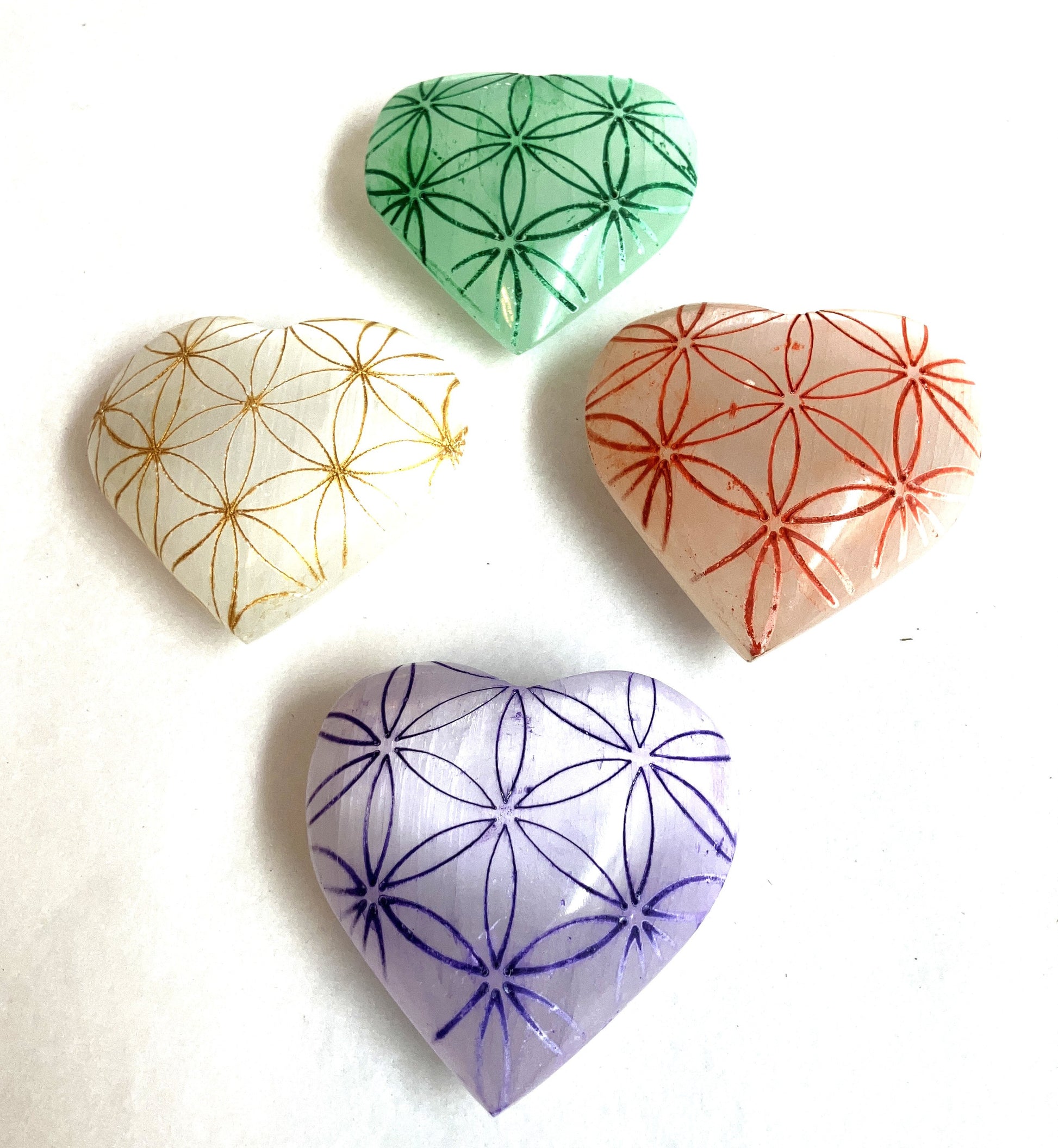 Four Selenite Etched heart-shaped stones with floral patterns in green, gold, red, and purple on a white background.