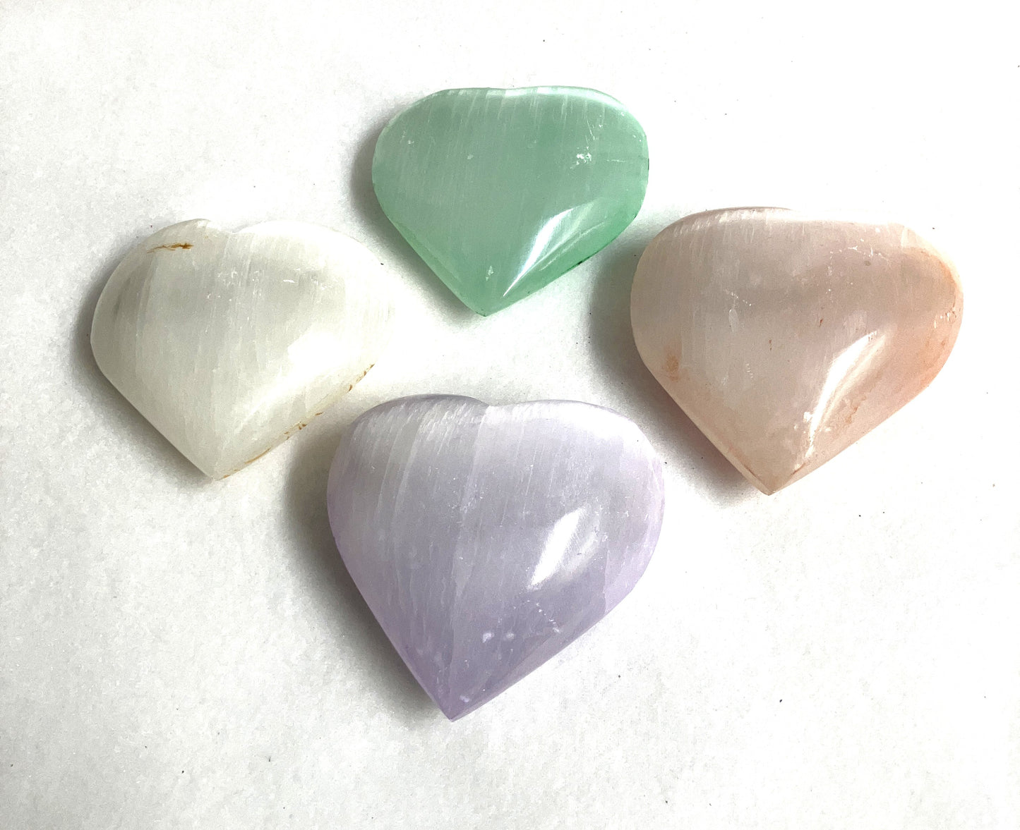 Four Selenite etched heart-shaped gemstones in white, green, pink, and purple showing the back-side.