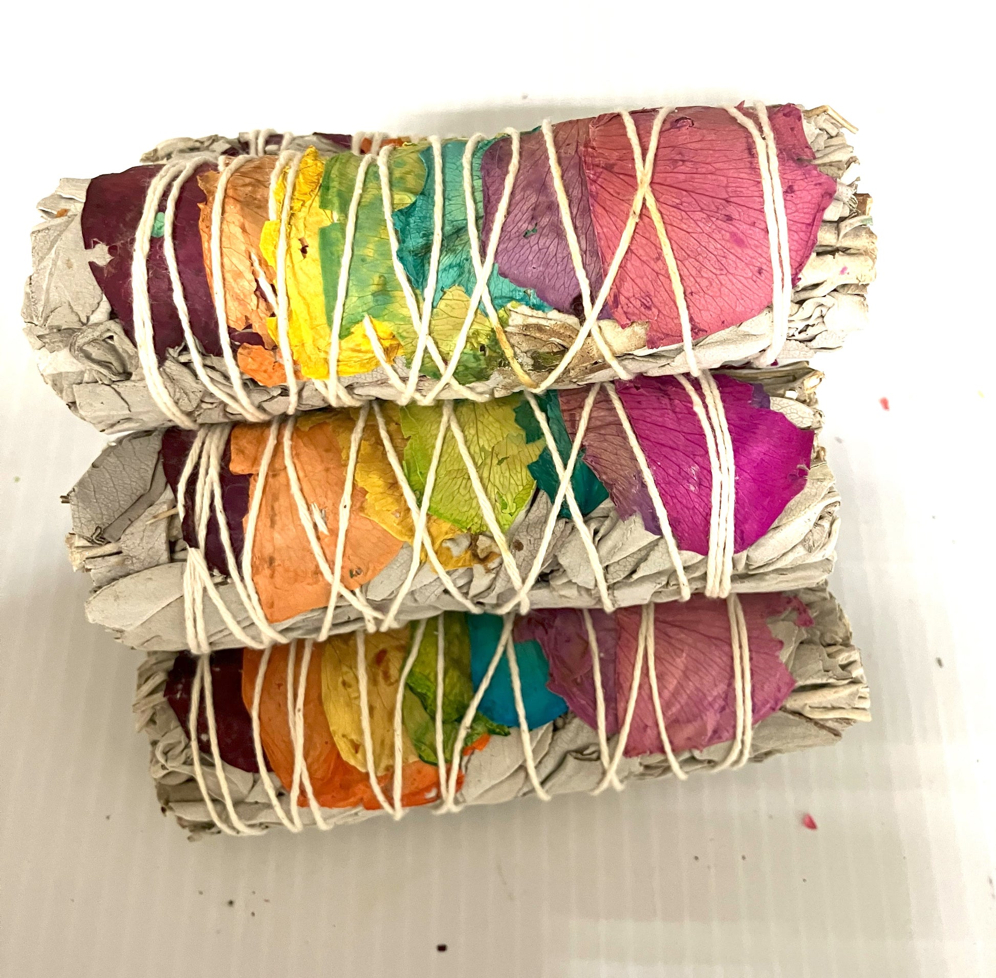 Stack of White Sage wrapped with colorful Rose Pedals and twine shown on a white background