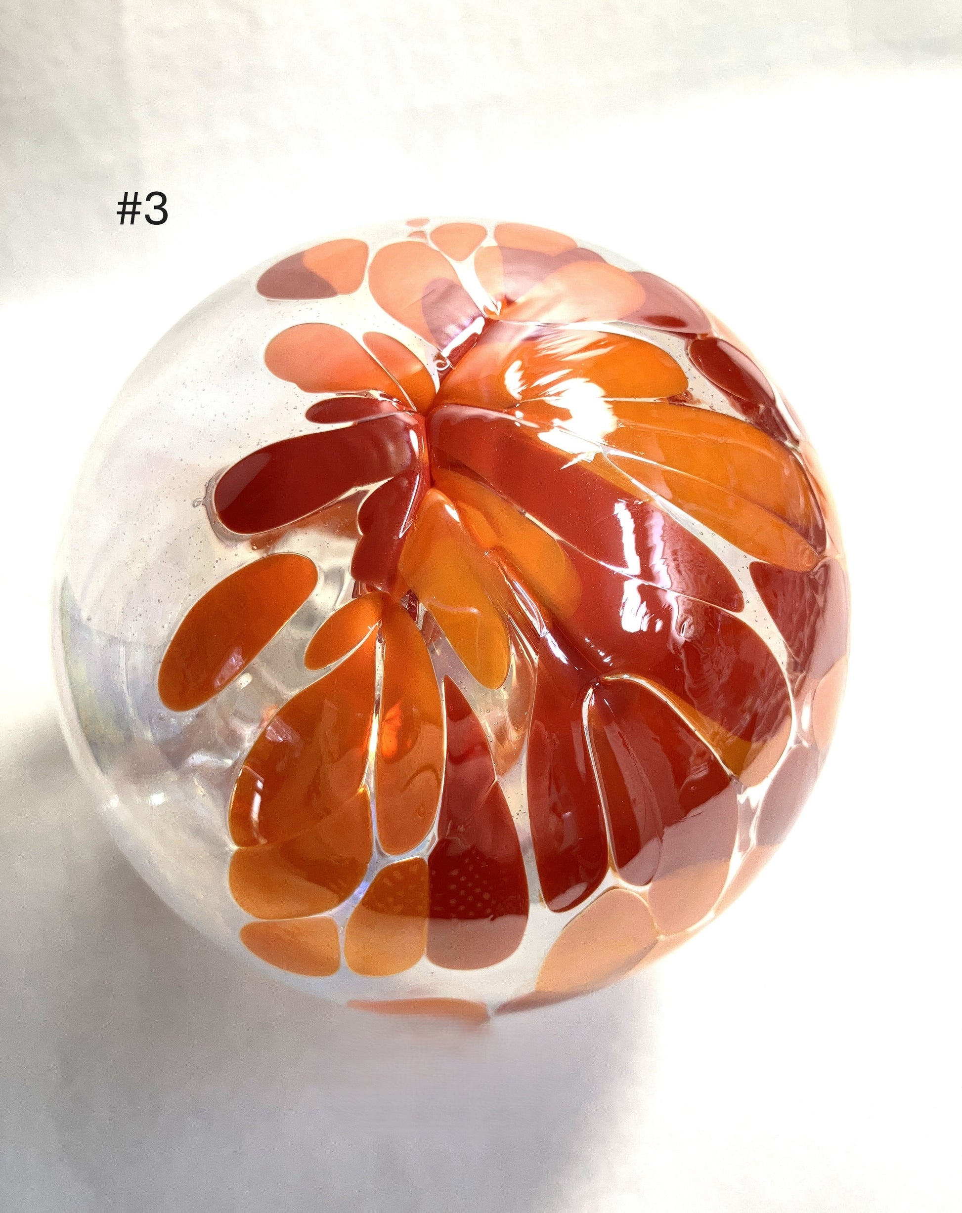Bottom of a Blown Glass Witch Ball with orange and red floral pattern on a white background