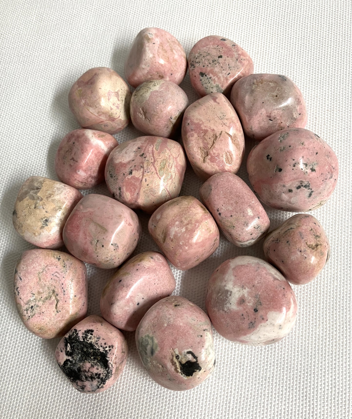 Tumbled Rhodochrosite Crystals showing stone variations on a light gray background