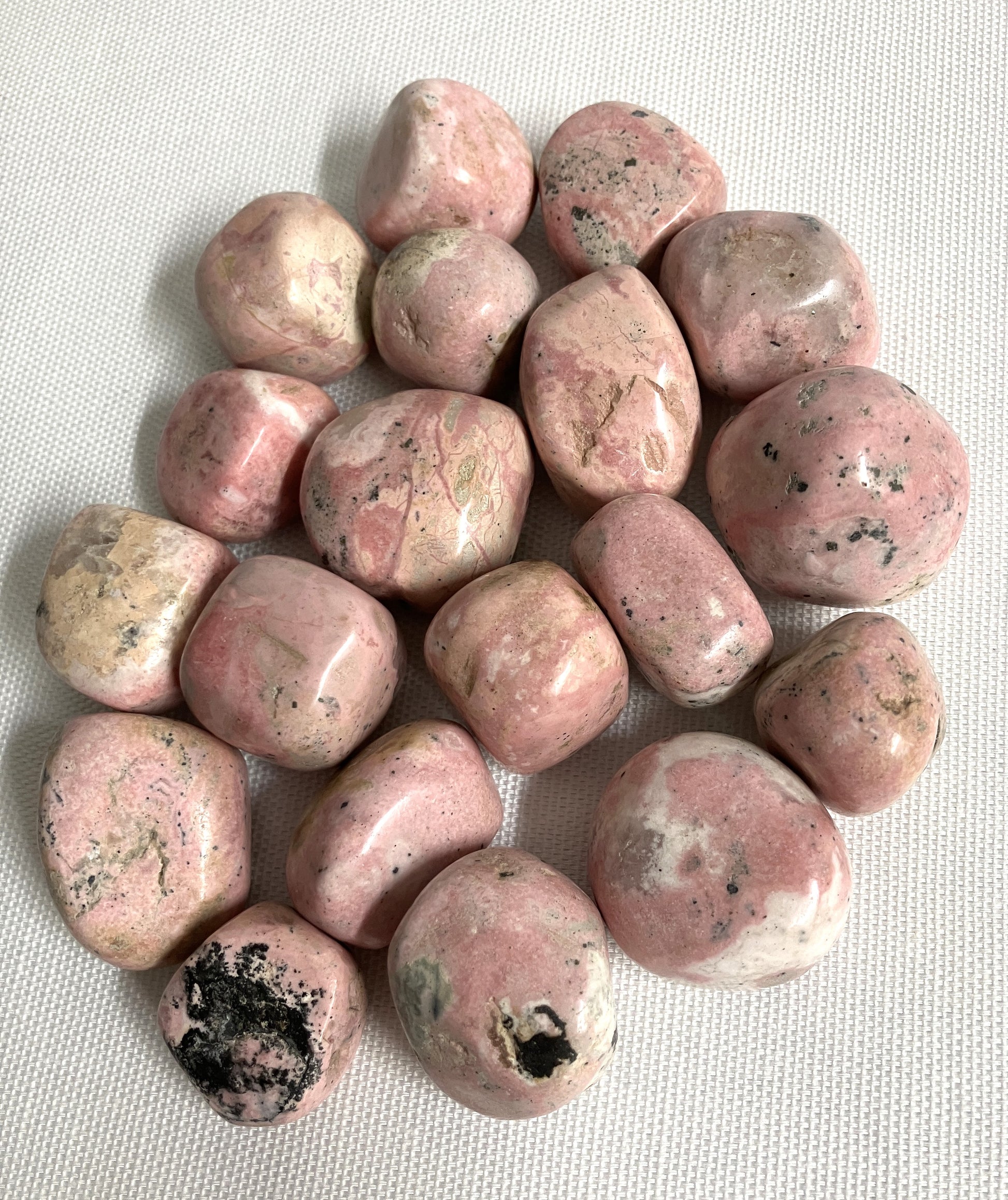 Tumbled Rhodochrosite Crystals showing stone variations on a light gray background