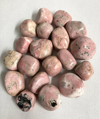 Tumbled Rhodochrosite Crystals showing stone variations on a light gray background
