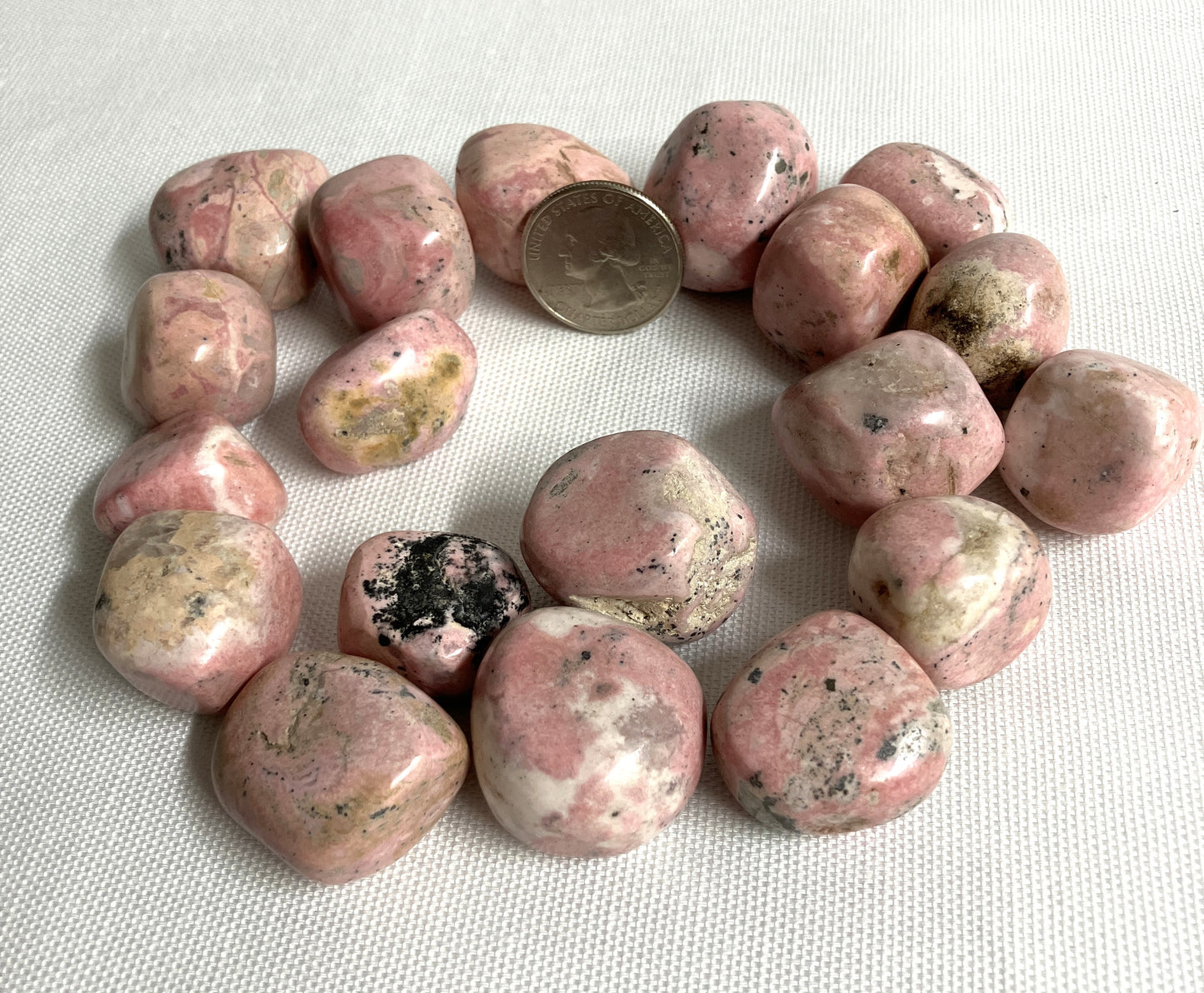 Rhodochrosite Crystals with a quarter for scale on a light fabric background