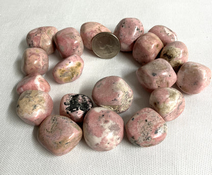 Rhodochrosite Crystals with a quarter for scale on a light fabric background