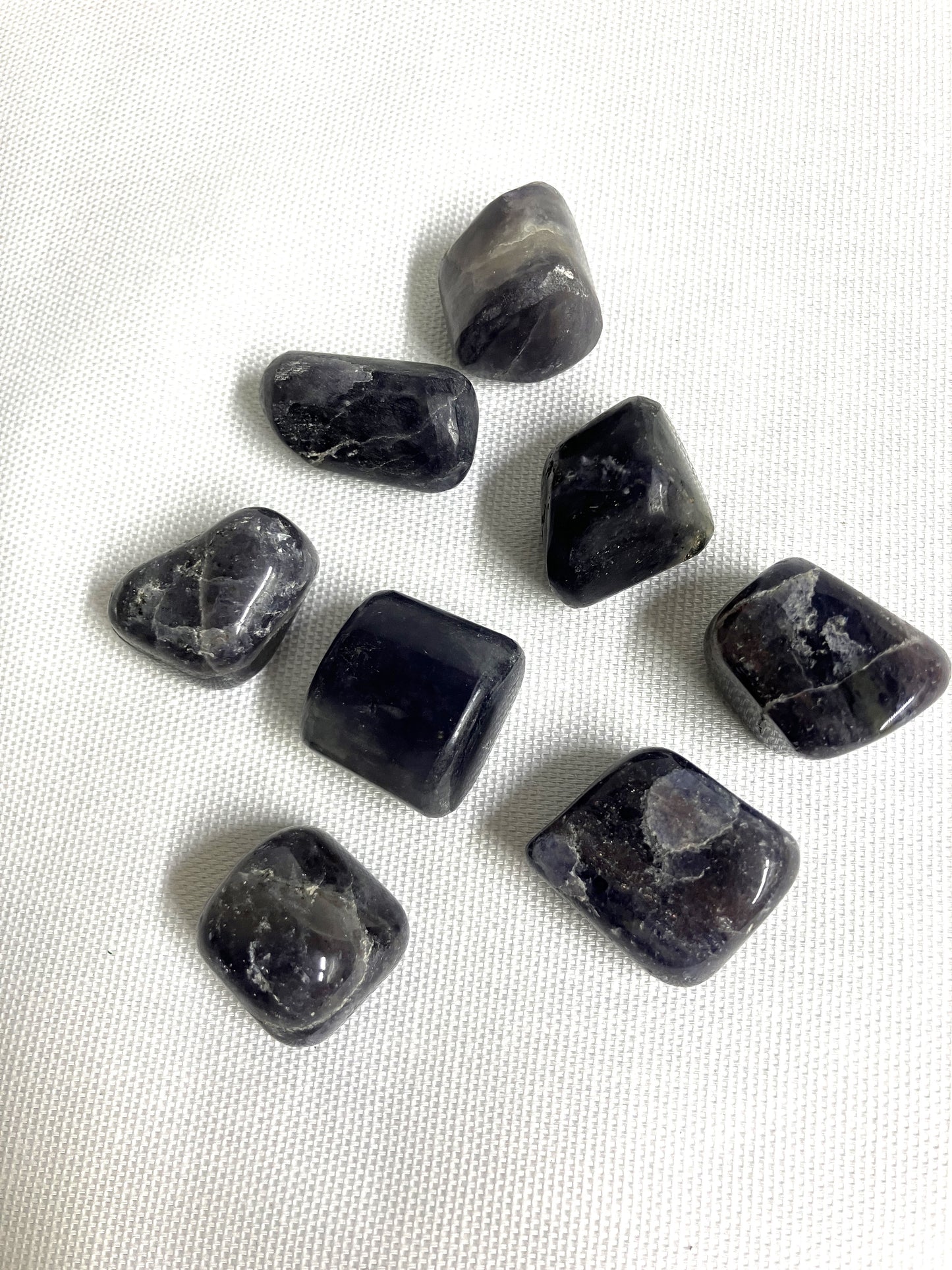 A group of seven Tumbled Iolite Crystals on a white fabric background