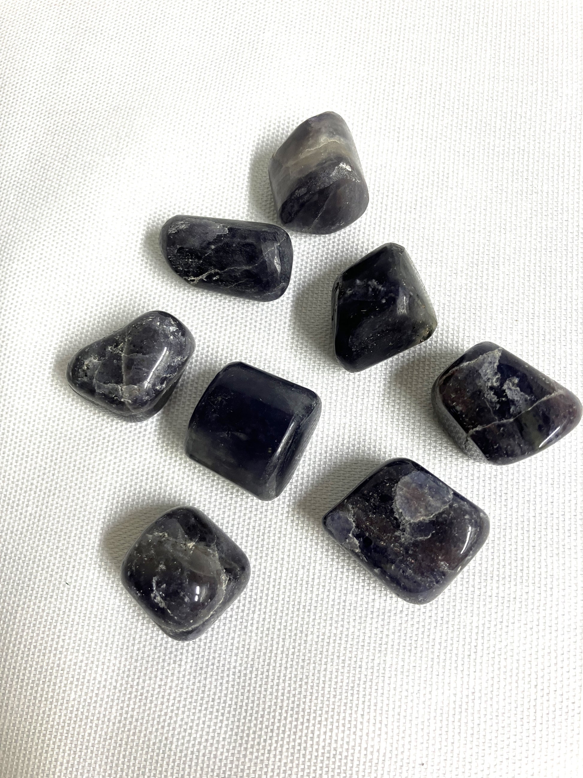 A group of seven Tumbled Iolite Crystals on a white fabric background