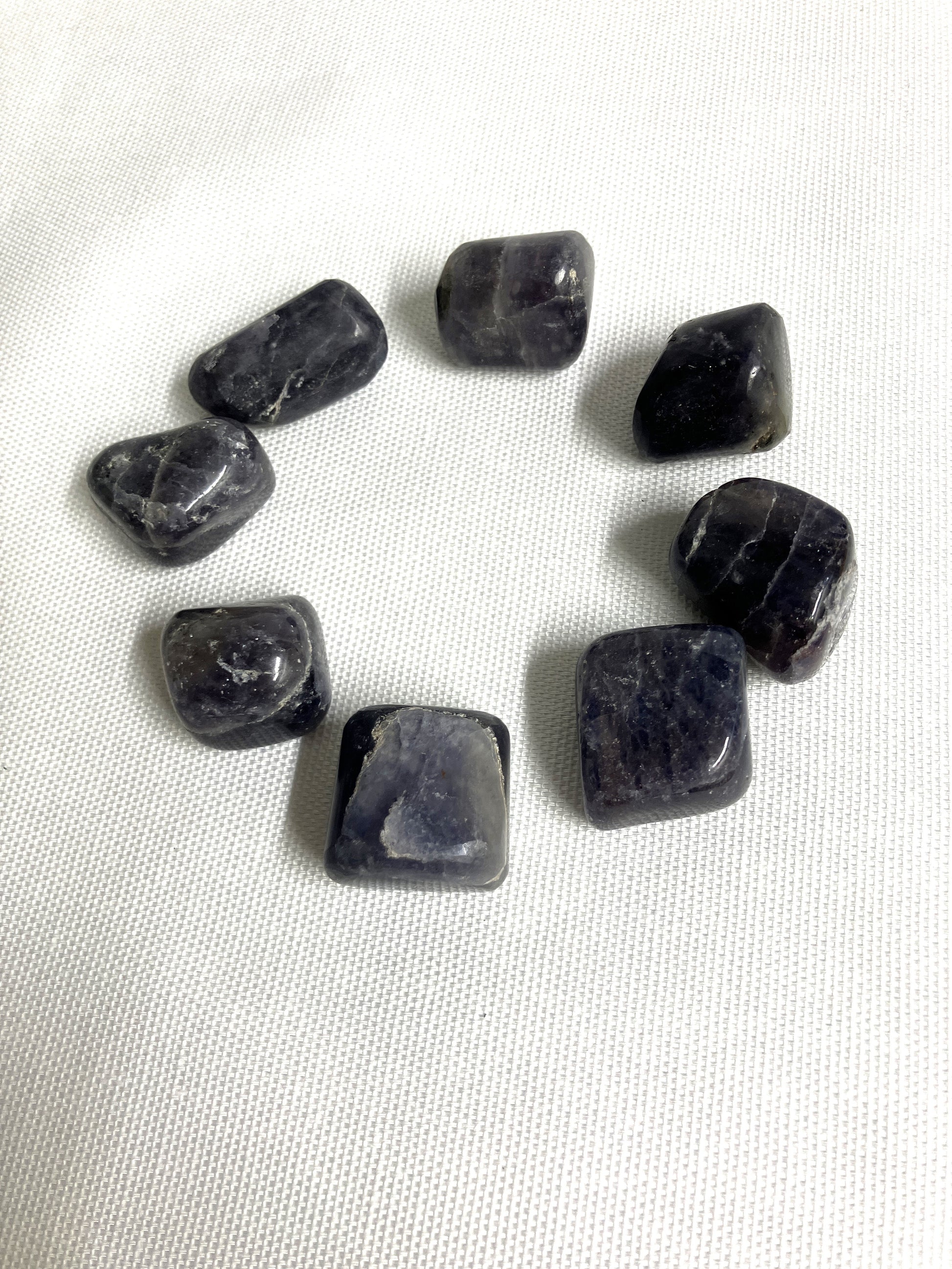 Tumbled Iolite Crystals arranged in a circle on a white fabric background