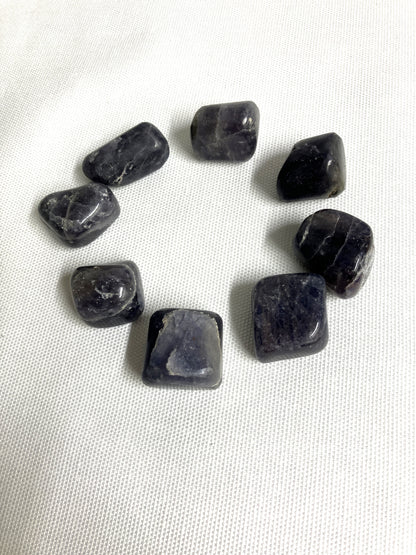 Tumbled Iolite Crystals arranged in a circle on a white fabric background