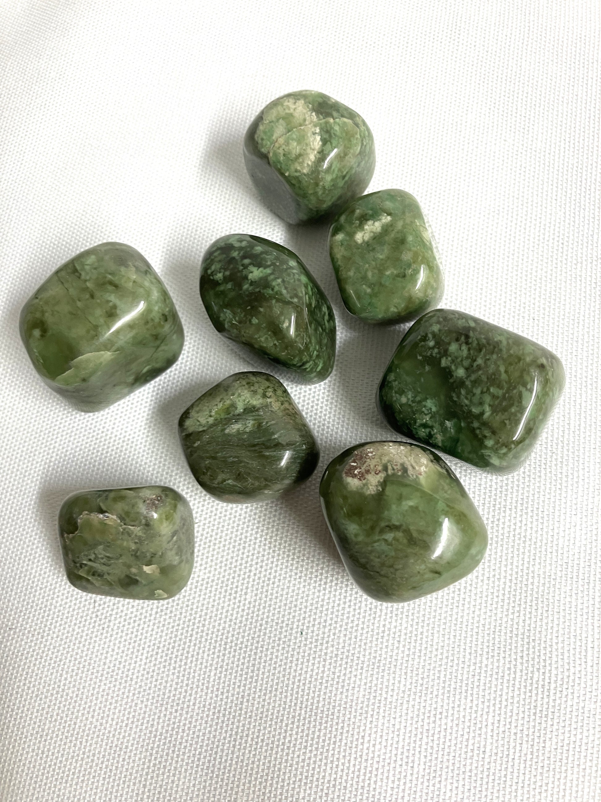 Tumbled Grossularite Crystal aka Green Garnet on a white fabric background