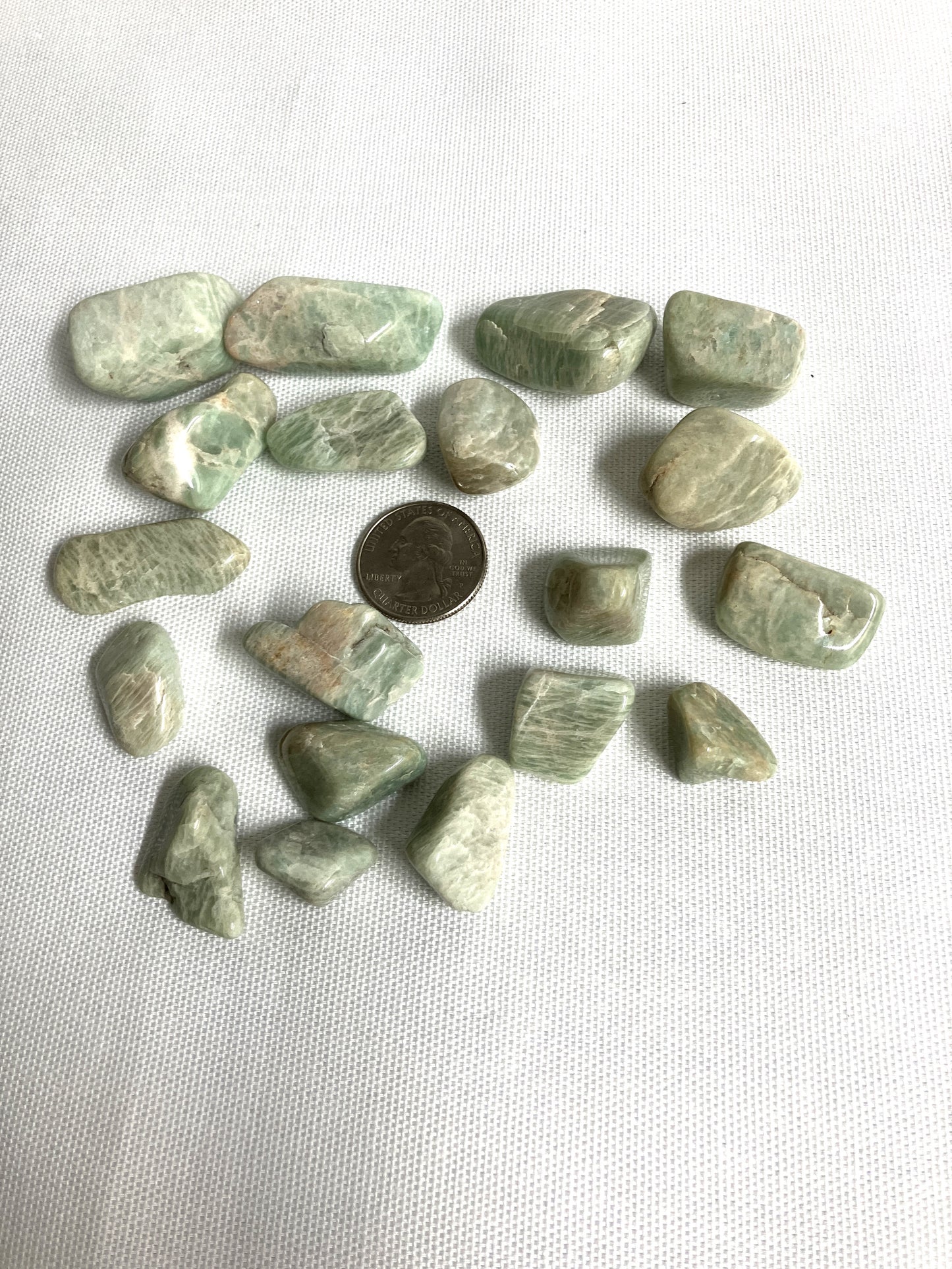 Tumbled Amazonite Crystals on a white background with a quarter for scale
