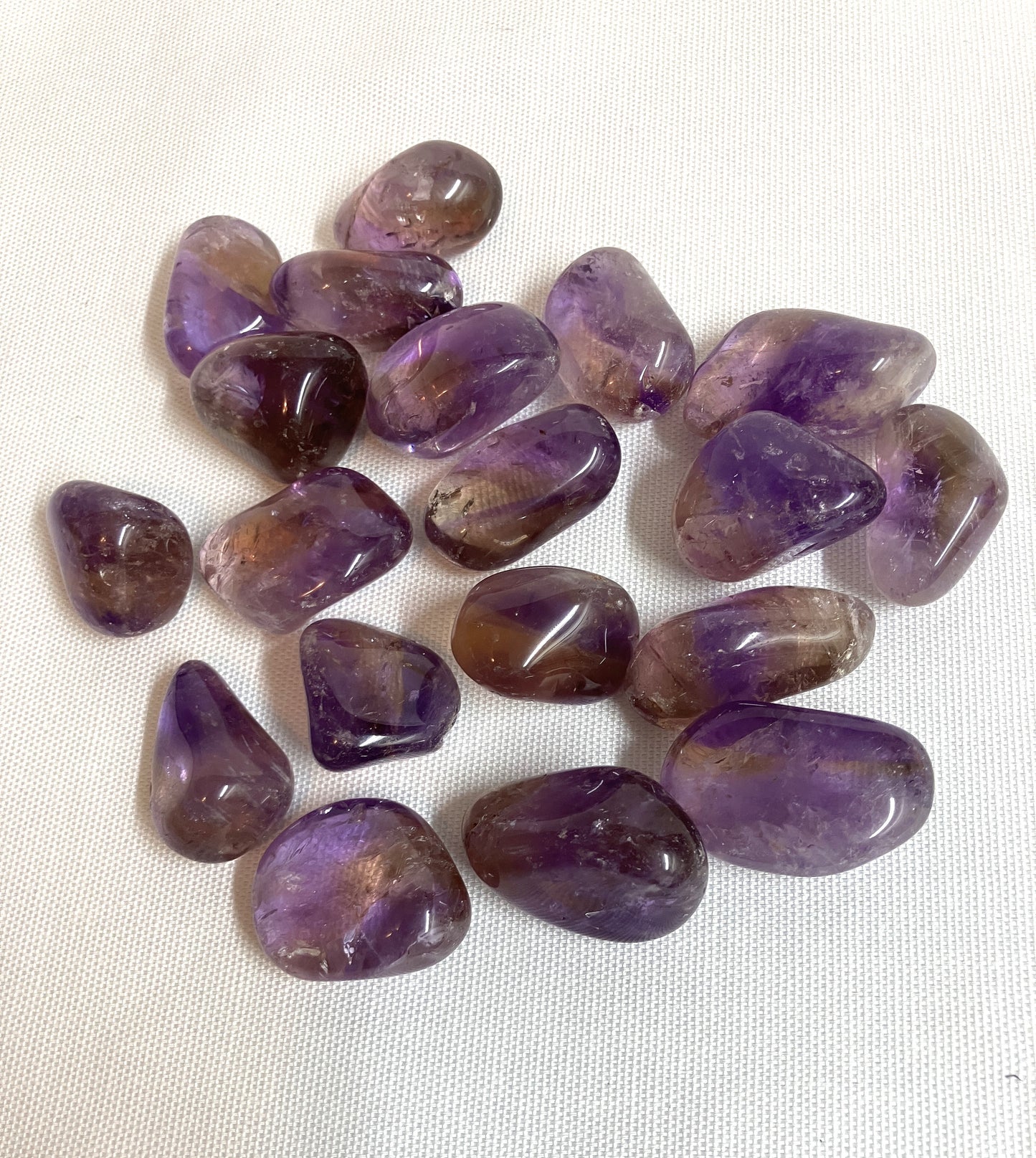 Top view of Ametrine Tumbled  Crystals on a white fabric background