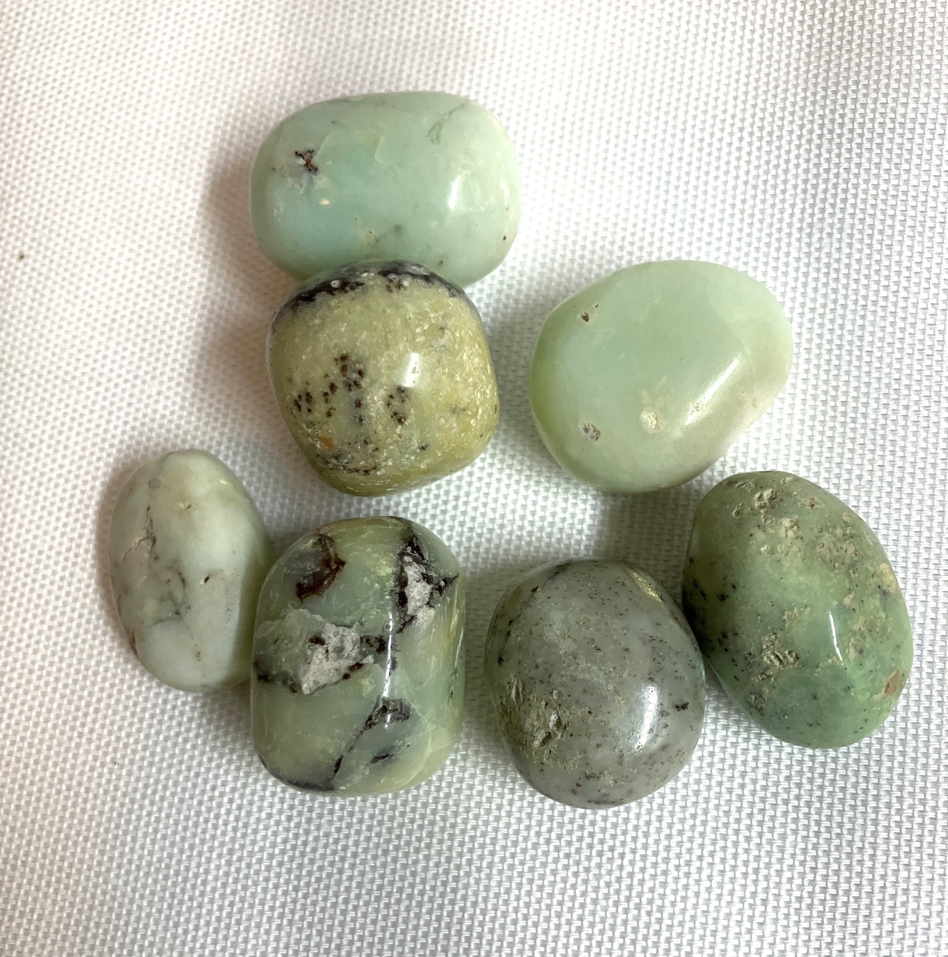 Green Chrysoprase Crystals Showing the unique pattern of many stones shown on a textured white surface