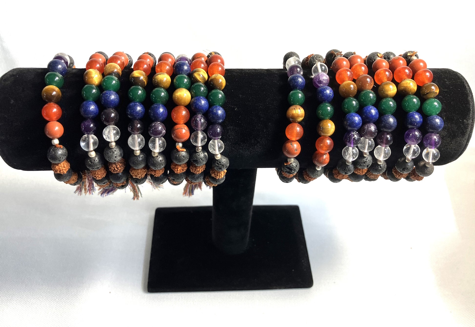 Chakra Stone Stretch Bracelet w/ Lava and Rudraksha Seeds on a black display stand against a white background
