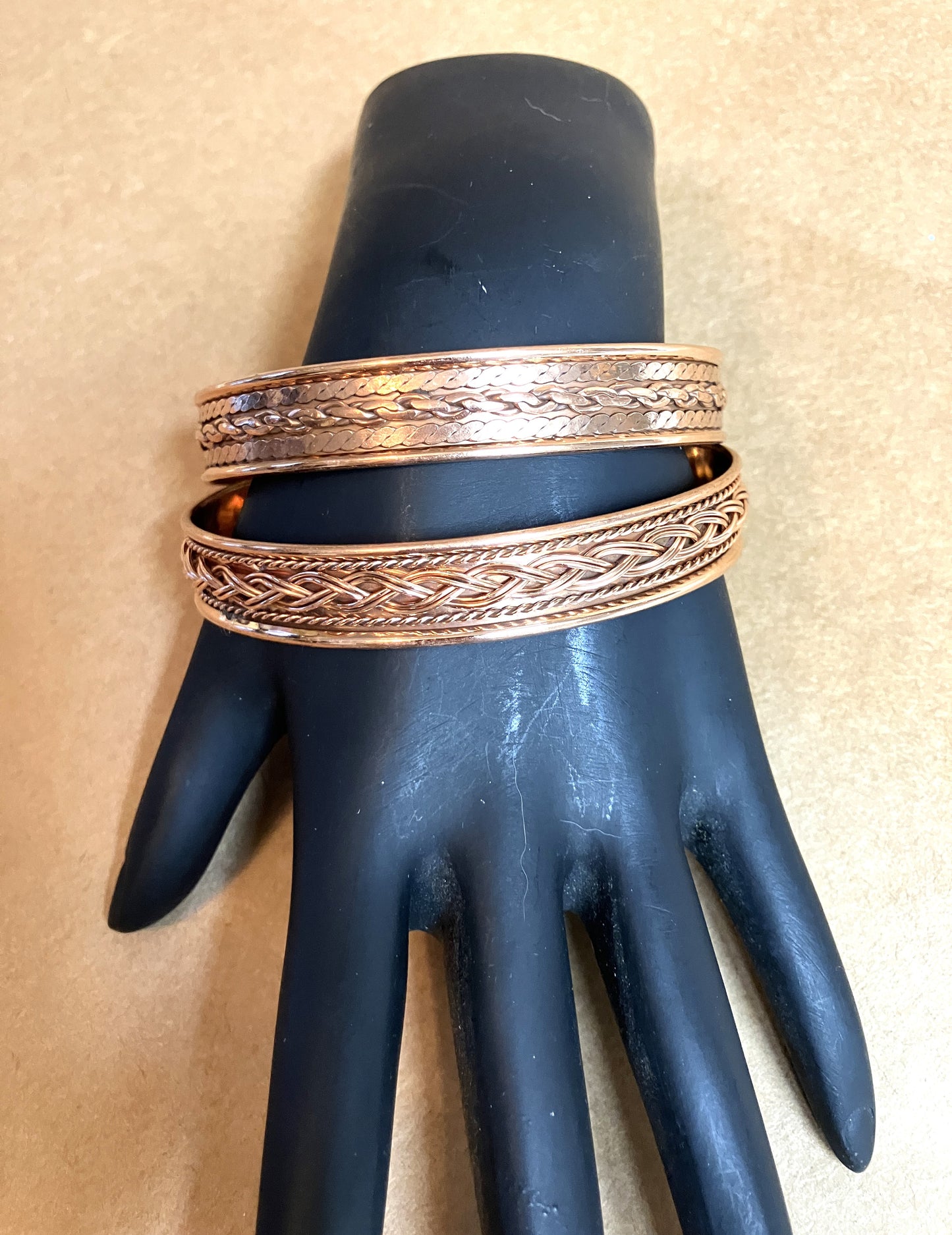 Two copper magnetic bracelets on a black mannequin hand against a beige background