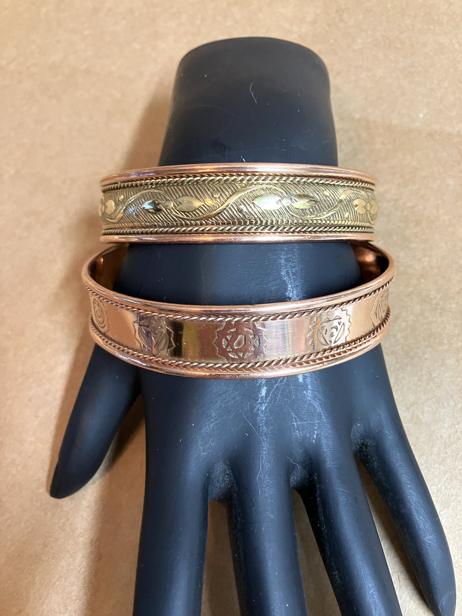 Two magnetic copper bracelets on a black mannequin hand against a beige background