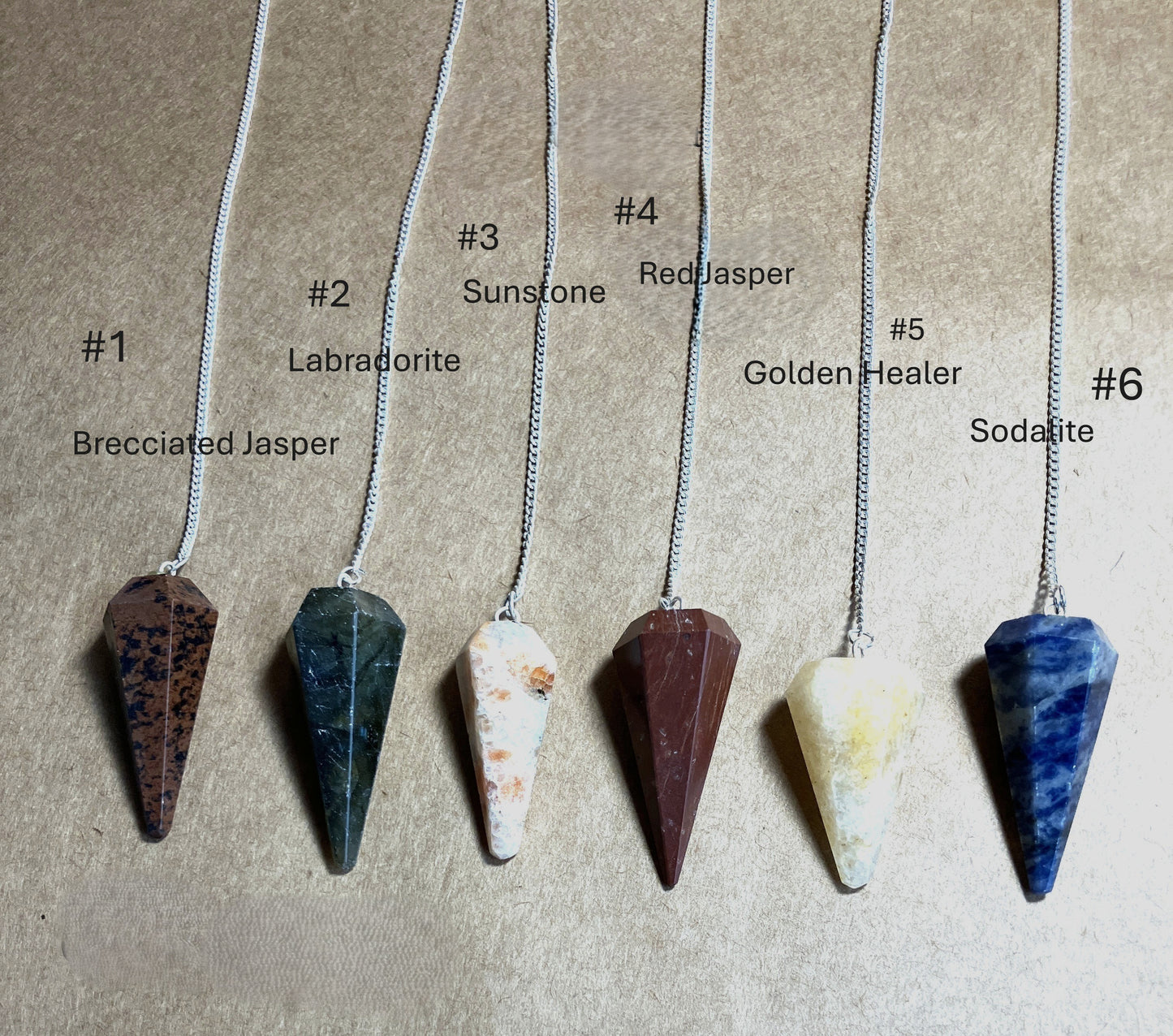 Six stone pendulums on chains with labels indicating stone type shown on a beige background