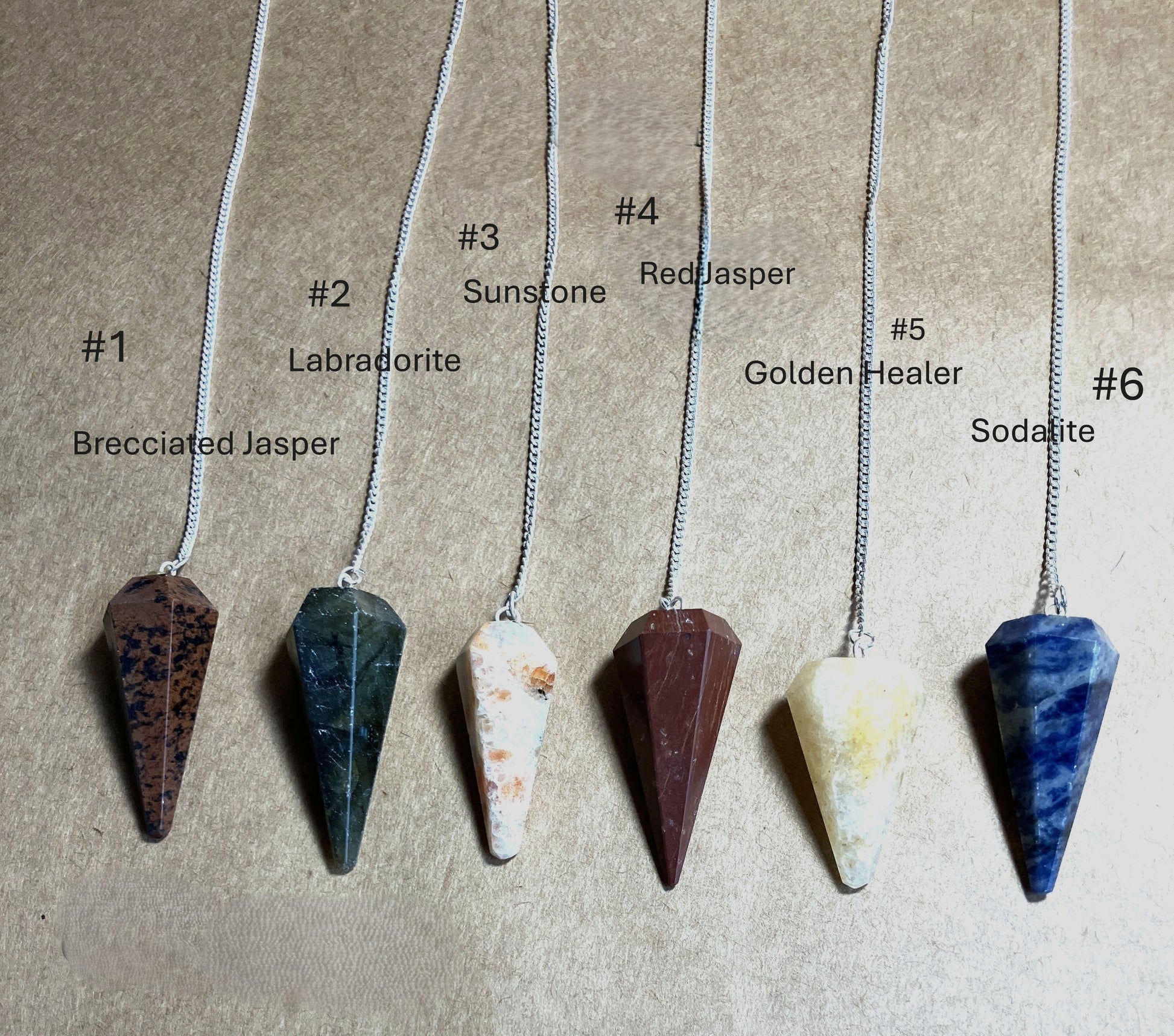 Six stone pendulums on chains with labels indicating stone type shown on a beige background