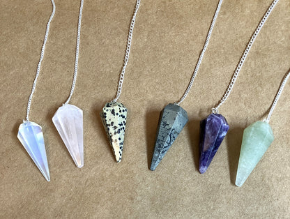 Six crystal pendulums on chains shown on a tan background