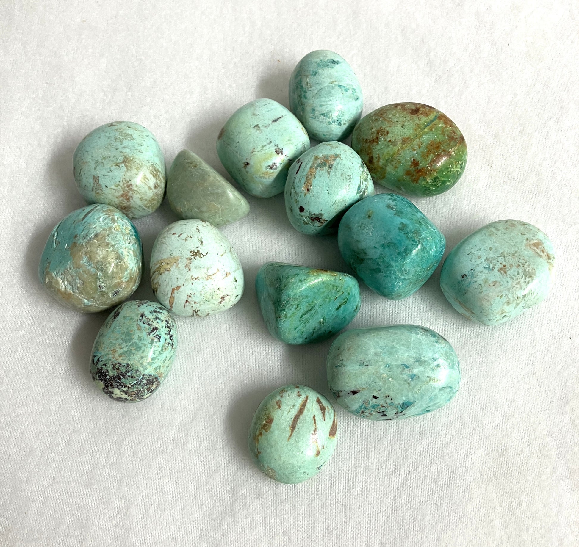 Group of Turquoise Tumbled Crystals from Peru showing various patterns and color variations on a white fabric background