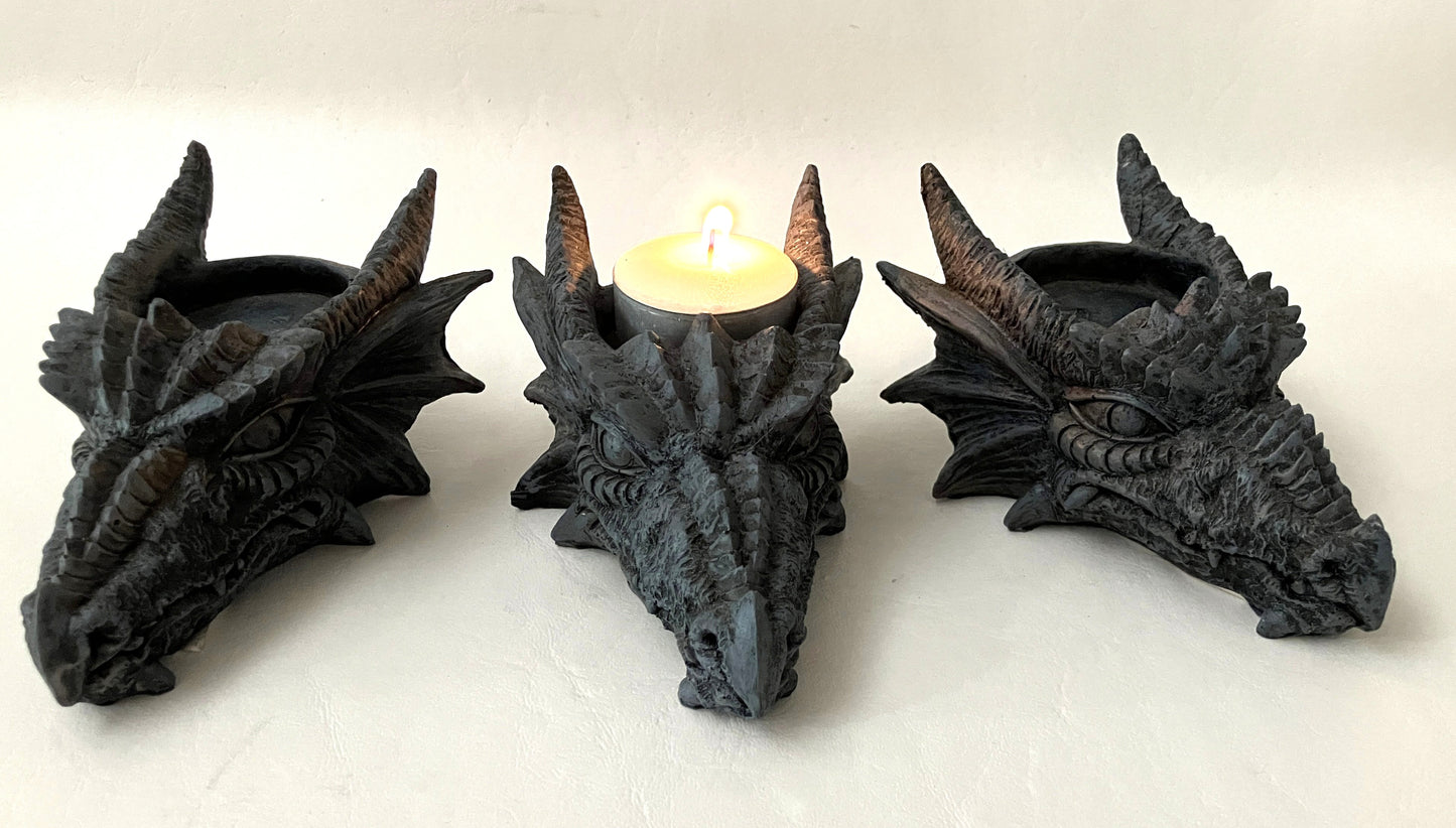Three dragon head candle holders with a lit candle in the center on a white background