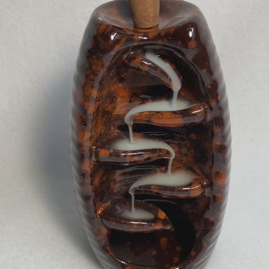 Brown bottle backflow burner shown with the smoke from the incense cascading down the front
