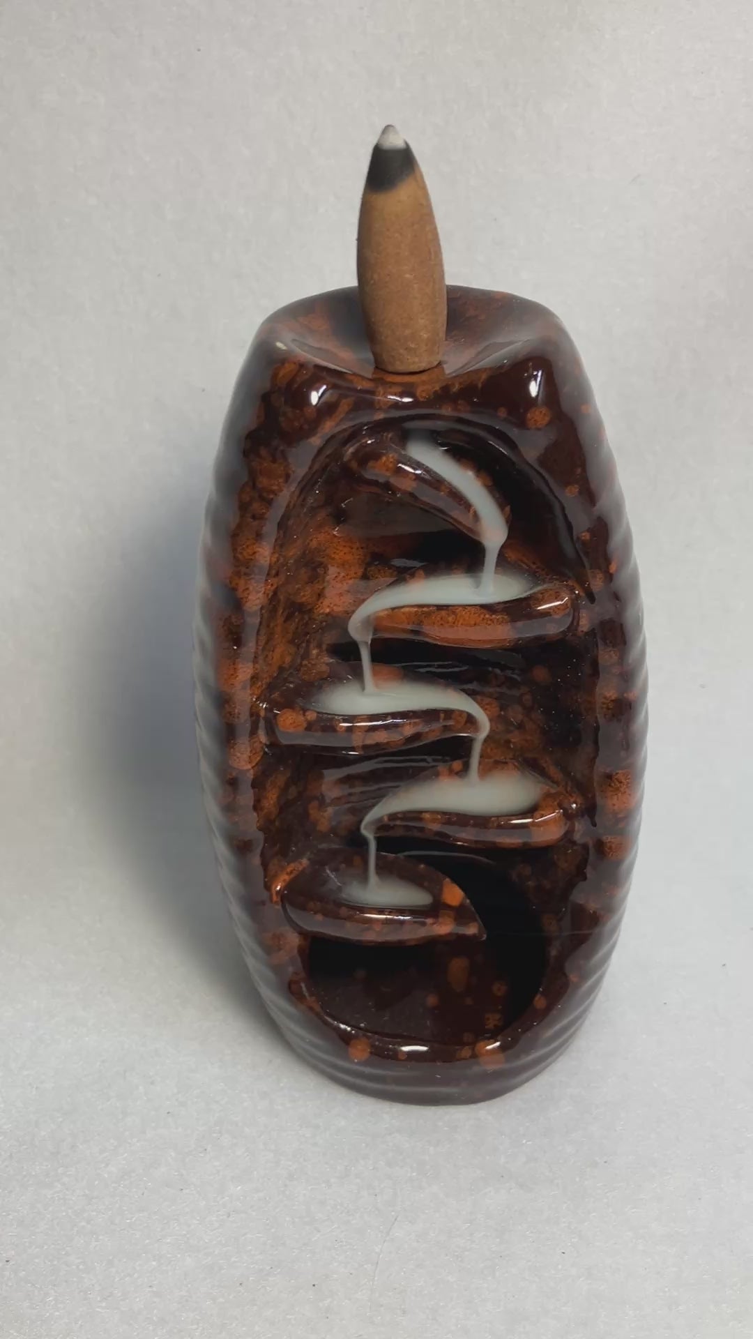 Brown bottle backflow burner shown with the smoke from the incense cascading down the front